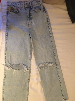 Jeans Gina tricot 34 - Säljer dessa jeans i modell idun wide. ljusblå och med hål. Strl 34, aldrig använda därmed i nyskick.