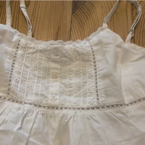 Vit sommartopp med fina detaljer - Säljer nu vidare detta linne köpt på plick pga alldeles för litet för mig. Passar xxs-xs. Fint skick, vet ej märke då lappen är bortklippt. 