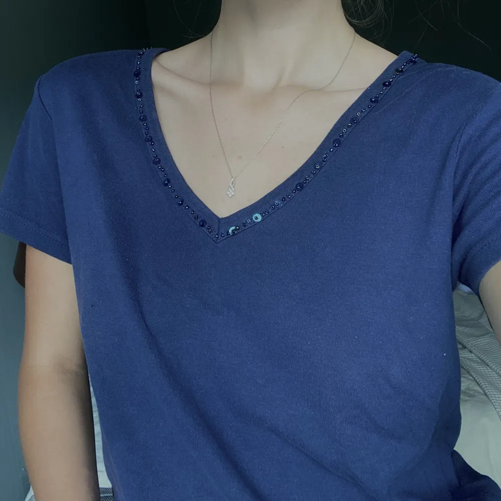 Mörkblå T-shirt med snygg pärldetalj, köpt secondhand och har en liten fläck strax under nyckelbenet men inget som stör!! Annars i bra skick🌷. T-shirts.