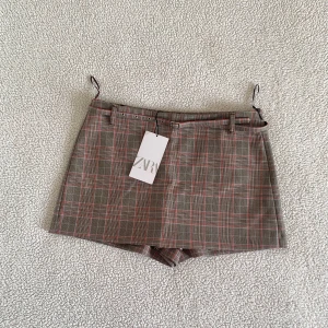ZARA rutig shortskjol med skärp (skorts) - Otroligt snygg lågmidjad shortskjol (skorts) från ZARA. Rutig brun / röd / ljusblå kjol med inbyggda shorts. Nya med tags kvar, utan anmärkningar.