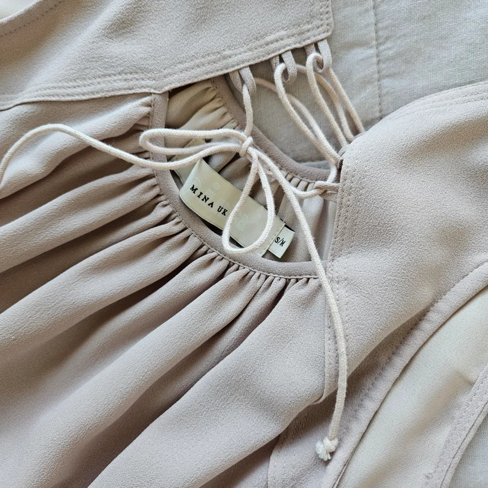 Kort, klockad modell med volang och knytning. Beige. Längd 85 cm. Storlek S/M. Mekot.