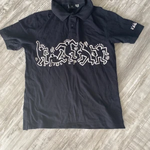 Piké  - Fint skick. Svart med vitt mönster fram och på ena armen 