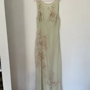 Balklänning, oanvänd med blommor på. Klänningen är en väldigt ljus nyans av grön och är mer åt de kräm vita hållet