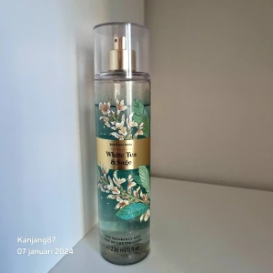 White Tea & Sage Fine Fragrance Mist - En fin doftmist från Bath & Body Works med doften White Tea & Sage. Flaskan är genomskinlig med en grön etikett dekorerad med vita blommor och gröna blad. Den har en spraypump och ett genomskinligt lock.