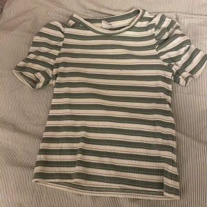 Randig topp från Lindex - En randig topp från Lindex i grönt och vitt. Toppen har korta ärmar och är tillverkad i ett ribbat material.