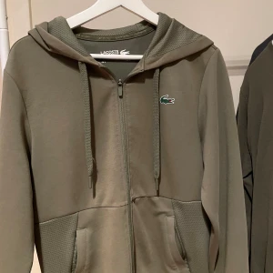 Lacoste zip up - Lacoste zip up i grön/oliv färg. Storlek S men passar också M. Inte använd mycket. Bra skick och bra kvalite. I sport material men passar till daglig användning. Vid funderingar hör av dig 🤝