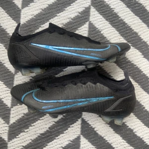 Nike Mercurial Vapor XIV Elite FG Svart Blå EU 42 - Skorna har använts men är absolut i bra skick. Dessa skor har inga snören med eftersom att snörena gick sönder. Dessa skor är väldigt svåra att få tag på. Pris kan diskuteras 