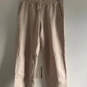 Beige byxor från Shein - Ett par beige byxor från Shein i storlek M. Byxorna har en elastisk midja med dragsko och är tillverkade av 100% bomull. De har en avslappnad passform och är bekväma för vardagsbruk.