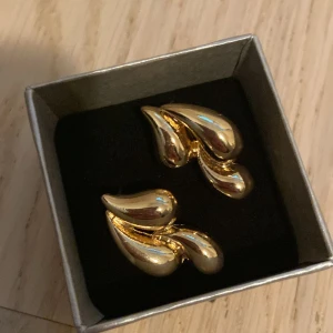 Guldfärgade örhängen - Ett par guldfärgade örhängen med en elegant, böljande form. 