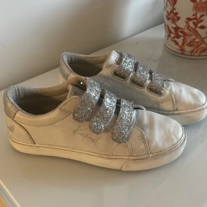 Vita skor från Kaporal - Jätte snygga vita skor med silver detaljer från kaporal som inte längre säljs i storlek 38. I bra skick, finns defekter under karborrebanden men det syns inte, designen är att de ska se lite slitna ut. Säljer för 300 och de inkluderar frakten.