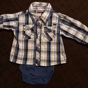 Skjortbody strl. 68 - Rutig skjortbody i storlek 68 från Hust. I fint skick, inga hål eller fläckar. Knappt använd.  Tvättad i parfymfritt tvättmedel och utan sköljmedel.