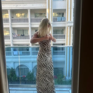 Zebramönstrad långklänning - En elegant zebramönstrad långklänning med djup urringning och öppen rygg. Klänningen är ärmlös och har en lös passform, vilket gör den perfekt för sommarens festligheter och även för event, fest. perfekta klänningen för allt! den är ny och knappt använd 