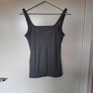 Ribbat linne - Ett ribbat, grått linne med lågt skuren rygg som get en smickrande look! 