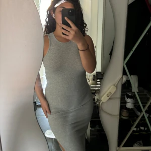 Grå ärmlös klänning - En grå ärmlös klänning med en tight passform. Klänningen har en slits på sidan och är lång. Från Jacqueline de Yong