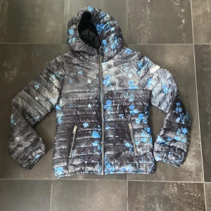 Jacka - En svart och blå pufferjacka från Diesel med ett blommigt mönster. Den är i strl 12 barn ( xs och s beroende på hur tight man vill ha den. Den är långärmad och har en huva . bra skick då den bara är använd en höst. perfekt som en höstjack