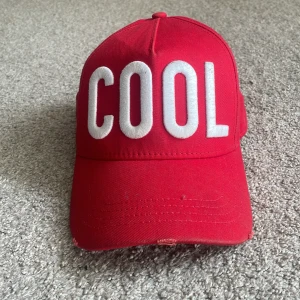 Röd keps från DSQUARED2 - En röd keps från DSQUARED2 med texten 'COOL' i vita bokstäver på framsidan. Köpt på nk i vintras och inte använt mycket sen dess (skick 9,5/10). Nypris: 1799 Meddela mig för frågor!