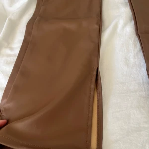 Skinn byxor  - Bruna skinnliknande byxor med slits från H&M. Aldrig använda med prislappen kvar. Storlek 40 men sitter tight på mig som har 36, byxorna går ner till marken. 