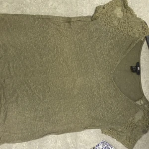 Olivgrön topp med spetsdetaljer - En olivgrön topp med spetsdetaljer på ärmarna. Toppen har en rund halsringning och korta ärmar.