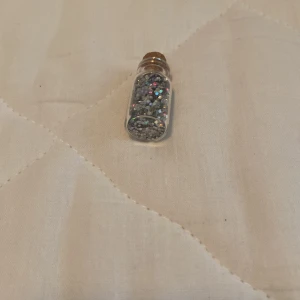 Glittrande ögonskugga i flaska - En liten flaska fylld med glittrande ögonskugga i olika färger. Perfekt för att lägga till en gnistrande effekt till din sminkning.