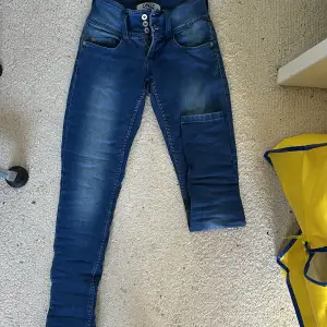 Säljer ett par snygga blå jeans från ONLY. De är i storlek Waist 27 och Length 32. Jeansen har en låg midja och är skinny fit. De har en dragkedja och tre knappar framtill. Perfekta för både vardag och fest!