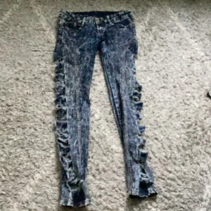 Blå jeans med slitningar - Säljer ett par blå jeans med coola slitningar längs benen. De är i en skinny fit och har en låg midja. Perfekta för en avslappnad och trendig look. Passar bra till både vardag och fest!