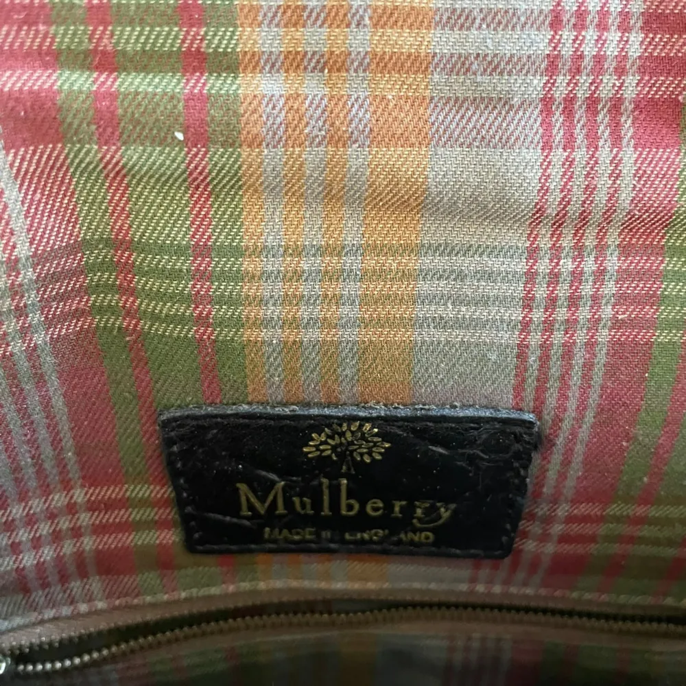 Säljer en snygg brun vintage (80-tal) axelväska från Mulberry. Väskan är gjord av skinn med en krokodilpräglad yta och har ett klassiskt rutigt foder i grönt, rött och orange. Den har en justerbar axelrem och ett spänne framtill. Insidan har en dragkedjeficka för extra förvaring. Perfekt för både vardag och fest!. Väskor.