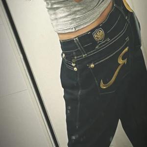 Mörkblå jeans från Rock & Republic - Säljer ett par snygga mörkblå jeans från Rock & Republic i storlek 27. De har en cool gul broderad logga på bakfickorna och en lågt midja. Jeansen är i bootcut-stil och har en klassisk femficksdesign med knappar och dragkedja. Köptes for 700kr 