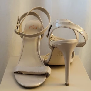 Sandaletter med 12 cm stilett, perfekta till studenten eller varma sommarkvällar ☀️ - En superfin och nätt sandalett med stilett som förlänger benen super fint!  Färgen är ljus lackad beige.  Perfekt till studentklänningen eller sommarkvällen.  Klacken är 12 cm. Se bild på slitage, sparsamt använda!