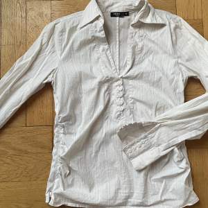 Vit, tight skjorta med textur och fina knäppningar🌟 På sidorna finns även dragkedjor så att man kan välja hur tajt den ska sitta. Köpt secondhand men i bra skick och utan tecken på användning. 