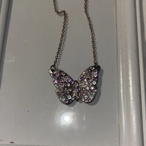 Halsband - Ett fjärilsbalsband från hm. Det är lite rostigt men det kanske kan tvättas bort? Annars är det bra skick. Färg- silver och lila och rosa diamanter/inte äkta
