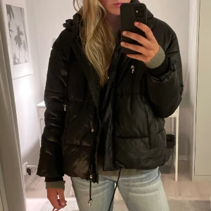 Svart vinterjacka  - Svart glansig jacka från Urban Outfitters med silvriga detaljer 