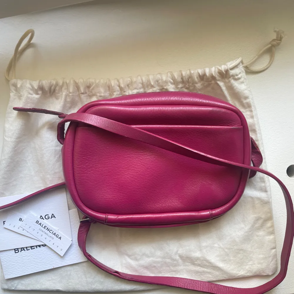 Säljer min coola Balenciaga väska i modellen camera bag i en rosa jätte fin färg! Väskan är flitigt använd därmed har den släppt lite i bandet (se bilder), men går att laga med textil limm. Till utseendet har den inga  defekter i färg osv.  . Väskor.