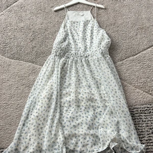 En klänning  - Den är 90 cm lång och är 35 cm bred. En lång sommarklänning i färgen vit med blå roser. Den är jätte bra skick 