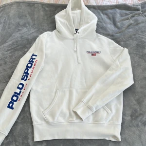 Polo Ralph Lauren vit hoodie - Vit hoodie från Polo Ralph Lauren i storlek S för herr. Har en pytteliten fläck uppe vid luvan men syns knappt om man inte står på väldigt nära håll. Fint tryck på ärmen med Polo Sport. 