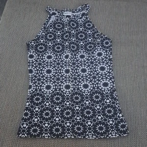 Svart och vit mönstrad topp - En svart och vit topp med ett blommigt mönster. Toppen har en hög hals och är ärmlös, vilket gör den perfekt för varmare väder.