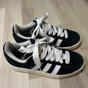 Adidas Campus 00s Skor - Nu säljer jag mina svarta Adidas Campus 00s skor eftersom att de är förstora. De är i bra skick då de bara har använts 4 gånger.   De är i storlek 38 2/3.  Man får även med extra snören i svart.  Hör gärna av dig vid frågor!