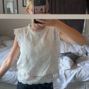 Vit spetsblus - En elegant vit spetsblus med detaljerade spetsmönster och volangkant vid ärmslut och nederkant.