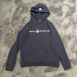 SailRacing Tröja - Det är en tjocktröja från Kidsbrandstore som har en ficka på magen och ett märke på luvan och framsidan. Den är mörkblå och stl 150. 