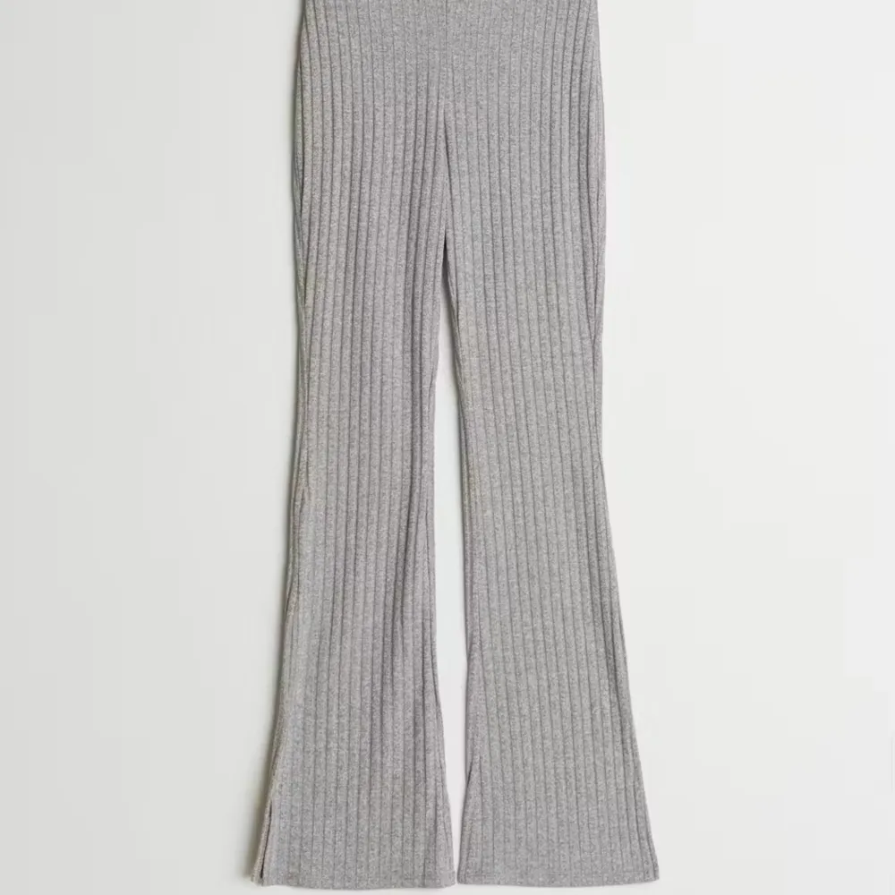 Tara Rib Trousers är ett par stilrena grå byxor med utsvängda ben. De är mycket bekväma och har ett elastiskt band i midjan för extra komfort. Byxorna är i storlek M och är figure hugging men också stretchiga, vilket ger en perfekt passform. . Jeans & Byxor.