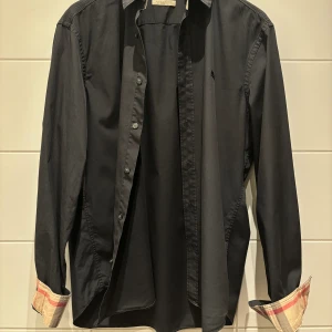 Burberry skjorta - herr - Burberry skjorta - herr Storlek L. Skjortan är sparsamt använd och har varker skador eller fettfläckar. Mer bilder finns tillgängliga om så önskas. Skjortan är givetvis autentisk. Frakt finns tillgängligt