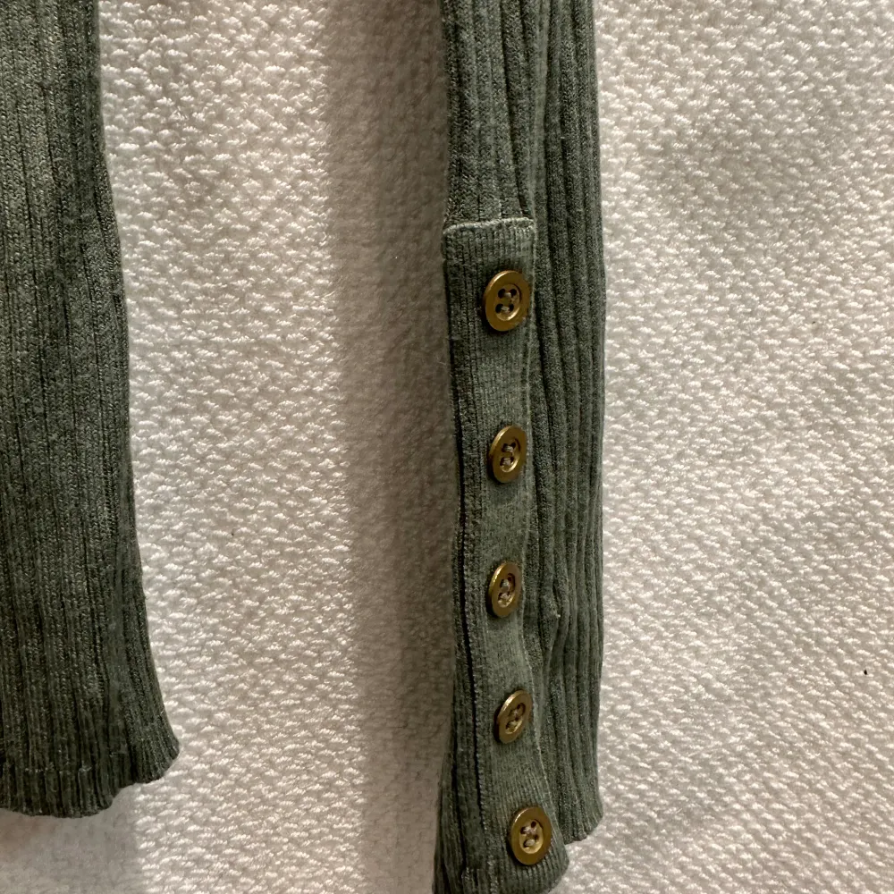 Grön stretchig polojumper med dekorativa knappar på ärmarna.   Strl: 8. Tröjor & Koftor.