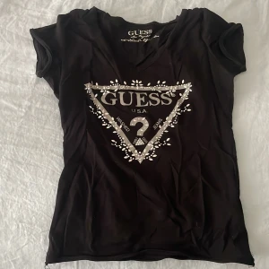 Guess Tshirt - Svart V-ringad T-shirt med silvrigt tryck från Guess säljes då den inte längre kommer till användning🖤