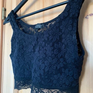 Croptop linne i spets - Sött croppat linne i svart spets från Topshop. Framsidan är stärkt med svart tyg, ryggen är genomskinlig. Märkt storlek 36. Fint skick! Längd 35cm Bredd 35cm