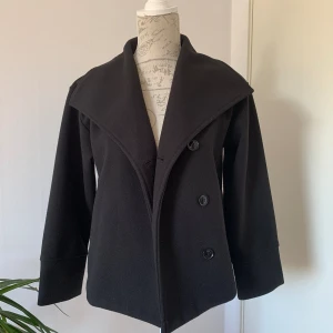 Gina tricot kort svart kappa - Skick: Mycket bra, använd ett fåtal gånger  Size: 146/152, dock är den stor i stl och är som en Xs/S.  Material: 100% polyester  Längd: Cirka 70cm 