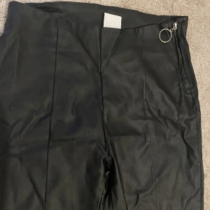 Helt nya svarta skinnbyxor med dragkedja på sidan. Nyskick läder byxa - Helt nya byxor i skinn/läder material med kedja på sidan. Skrynkliga för att de varit vikta. 