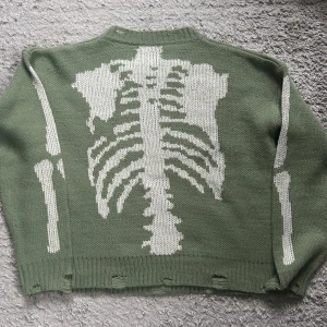 Skelett tröja  - Grön skelett tröja som jag köpte här på Plick men som tyvärr inte kommer till användning. Skelettet är på baksidan. Hålen är en del av designen och var där när jag köpte den :) står ingen storlek men skulle säga M