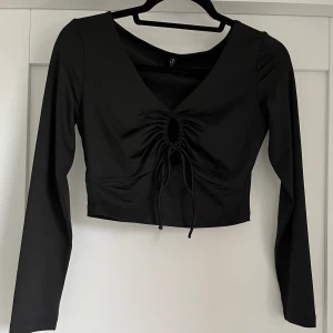 Svart långärmad tröja med  - Svart långärmad tröja med öppen urringning, går att justera öppningen med banden. Köpt utomlands och har endast använt 2 gånger.