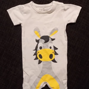 Playsuit/jumpsuit giraff strl. 62 - Playsuit/jumpsuit/onesie i strl. 62. I fint skick, inga hål eller fläckar. Ser knappt använd ut sånär som på att det finns sprickor i trycket nere i grenen. Syns främst när tyget tänjs ut. Unisex  Tvättad parfymfritt, utan sköljmedel 