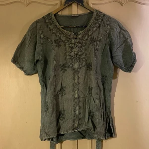 Grön tröja  - Grön tröja med fina broderier. Går att knyta på baksidan. Saknar storlek men skulle säga att den passar S-L beroende på hur en vill att den ska sitta. Så fin och i bra skick men säljer för att den tyvärr inte kommer till användning. 