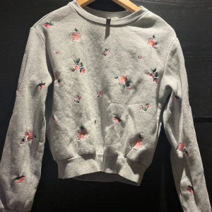 Sweatshirt  - Grå sweatshirt med broderade blommor på framsidan. Lite croppad.